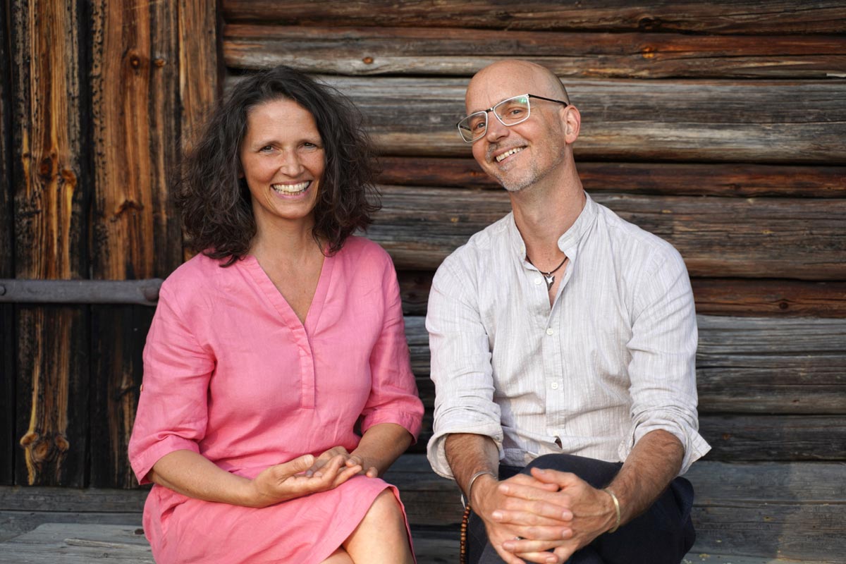 Britta Weber und Wolfgang Walch sitzen vor einer Holzhütte